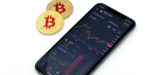 Smartphone displaying Bitcoin trading chart alongside two physical Bitcoin tokens.