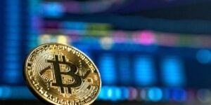 A golden Bitcoin coin in sharp focus against a blurred backdrop of trading charts