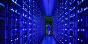 A technician walking through a dimly lit corridor of a cryptocurrency mining farm, surrounded by rows of glowing mining rigs