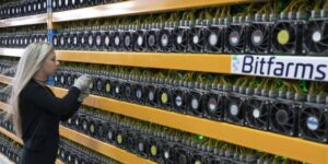 A technician working in a large-scale cryptocurrency mining farm, inspecting rows of mining rigs at Bitfarms.