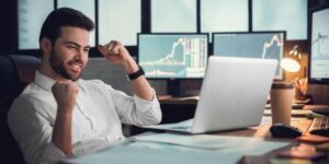 Man celebrating success while learning how to invest in crypto, with financial charts on screens in the background.