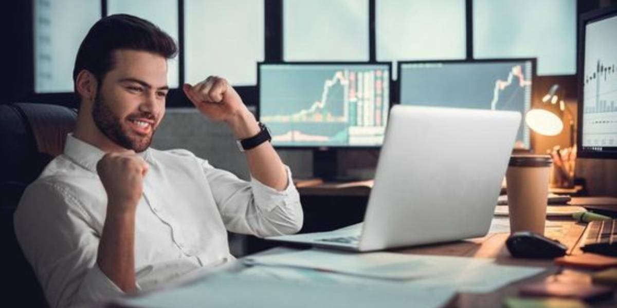 Man celebrating success while learning how to invest in crypto, with financial charts on screens in the background.