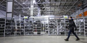 Large cryptocurrency mining facility with rows of mining rigs and a technician walking by
