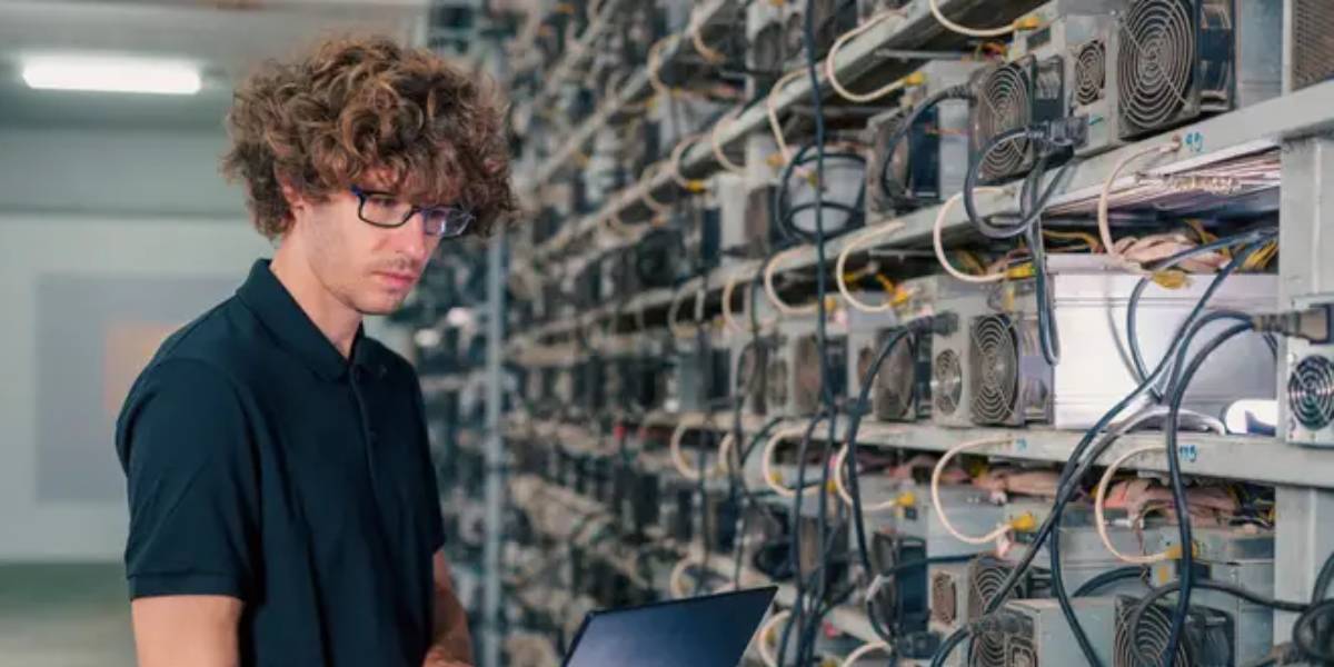 Technician inspecting Bitcoin mining hardware in a data centre with ASIC miners.