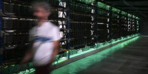 Person walking past rows of cryptocurrency mining rigs in a large facility.