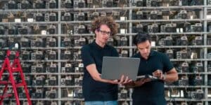 Two technicians inspecting cryptocurrency mining rigs at a miner hosting facility