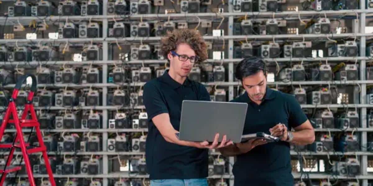 Two technicians inspecting cryptocurrency mining rigs at a miner hosting facility