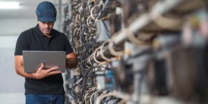 Technician inspecting mining rigs in a cryptocurrency data centre using a laptop.