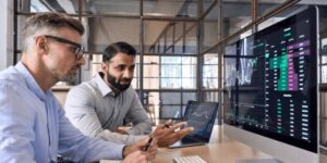 Two professionals analysing charts on multiple screens discussing the fundamentals of the crypto market