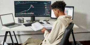 Young trader studying a book in front of crypto charts on multiple monitors focused on mastering market cycles 