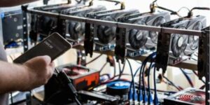 Person checking cryptocurrency mining performance on a smartphone beside a custom-built GPU mining rig.