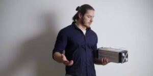 Person holding an ASIC miner while evaluating considerations in bitcoin mining.
