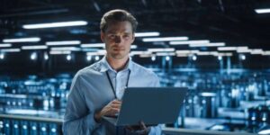 Technician using a laptop in a data centre, monitoring bitcoin cloud mining infrastructure and server performance.