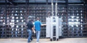 Technicians inspecting rows of Bitcoin mining rigs inside a large cryptocurrency mining facility.