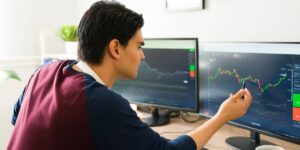 Man analysing cryptocurrency charts on dual monitors for crypto investing.