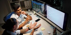 Two people reviewing cryptocurrency market data and Bitcoin dominance charts on desktop screens.