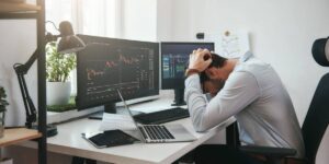 Man stressed while reviewing cryptocurrency trading charts on multiple screens.